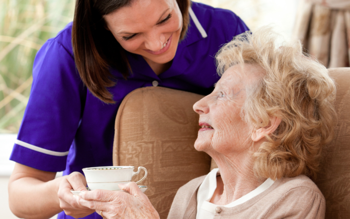 care assistant providing home care, handing a tea cup to a service user in a home setting