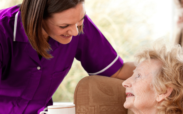 care assistant offering service user a warm drink in home setting